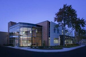 A picture of SARTA's Main Office at Gateway. Modern building with large glass windows and a combination of brick and metal paneling, illuminated with a tree in the background