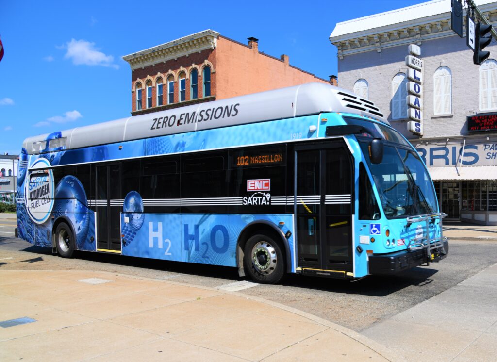 Route 102-Blue hydrogen bus heading into Cornerstone- A SARTA hydrogen fuel cell bus with a blue 'Zero Emissions' wrap that is at a stop light in downtown Canton. This bus design features water molecule graphics and the chemical formula 'H₂O' to emphasize its eco-friendly technology.