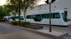 Hydrogen Street Car Prototype-Futuristic white streetcar with a sleek, modern design parked along a landscaped walkway with trees and a contemporary building in the background.