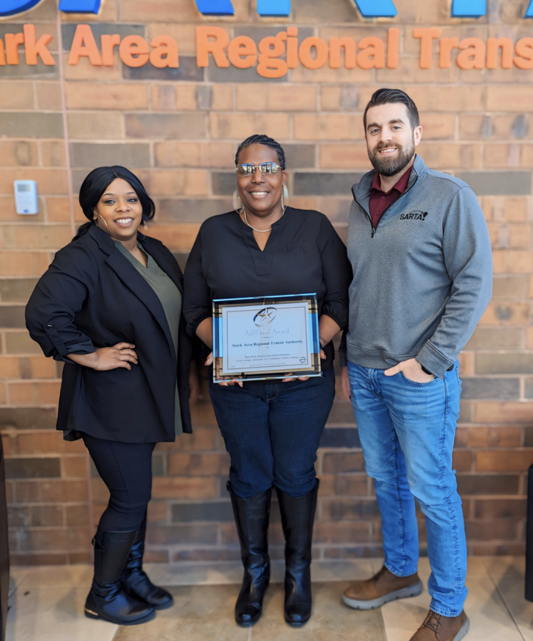 image features members of the SARTA Marketing Team posing with an AdWheel Award. The setting appears to be inside a SARTA facility, with the organization's branding visible in the background. The AdWheel Awards, presented by the American Public Transportation Association (APTA), recognize excellence in marketing and communications in the transit industry.
