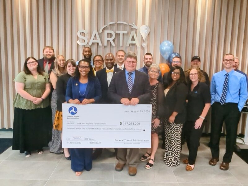 image captures a celebratory moment at SARTA’s Grand Opening & Grant Award event on August 15, 2024. The SARTA team and partners are gathered with a large check from the Federal Transit Administration for $17,254,229, signifying a major investment in public transportation.