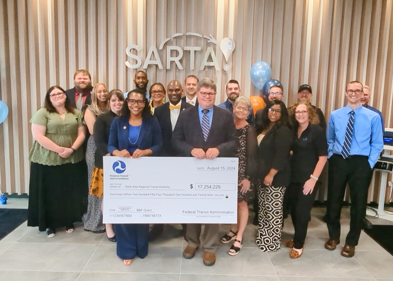 image captures a celebratory moment at SARTA’s Grand Opening & Grant Award event on August 15, 2024. The SARTA team and partners are gathered with a large check from the Federal Transit Administration for $17,254,229, signifying a major investment in public transportation.